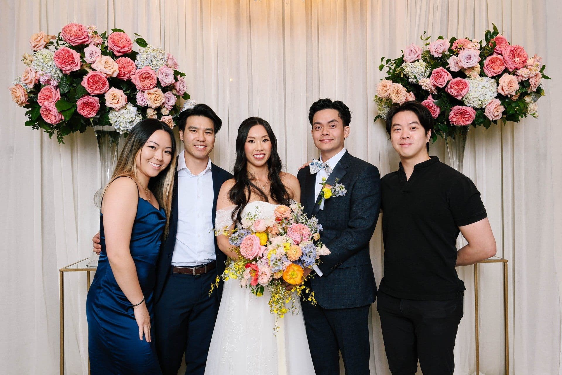 A newly married couple with the Radiate team in front of a floral wedding backdrop